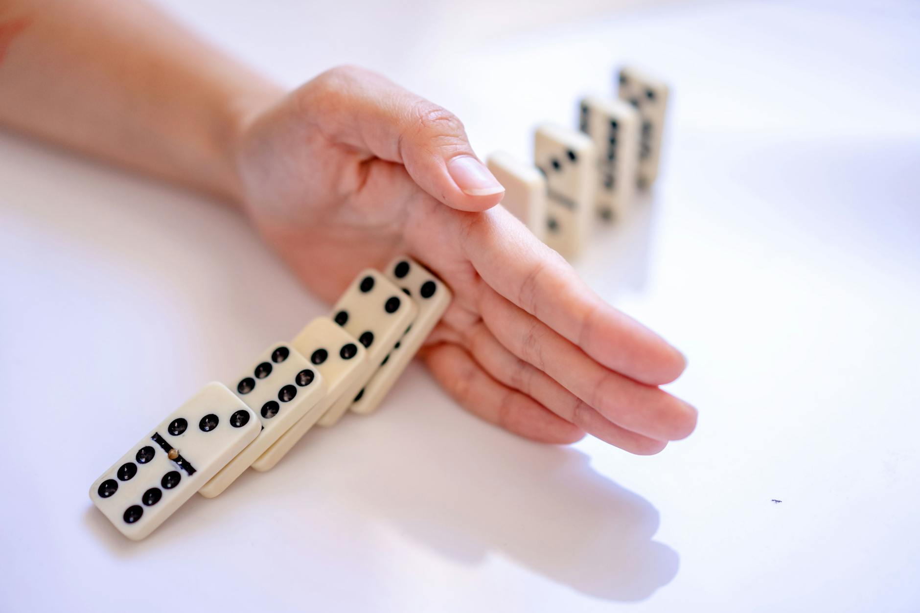 A hand stopping the domino effect, captured on a white background, symbolizing control.
