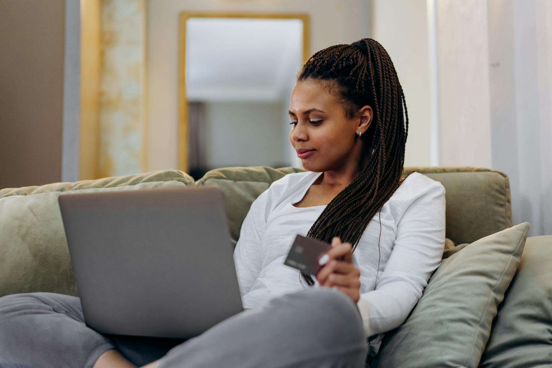 Woman sitting on a couch shopping online with a laptop and credit card.